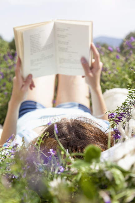 Giovane donna sdraiata sul campo lettura libro — Foto stock