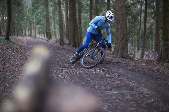 Ciclista en pista de tierra forrada de árboles con casco de ciclismo cayendo de la bicicleta - foto de stock