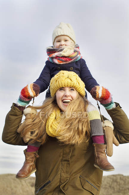 Femme souriante mi-adulte portant sa fille sur les épaules de la côte — Photo de stock