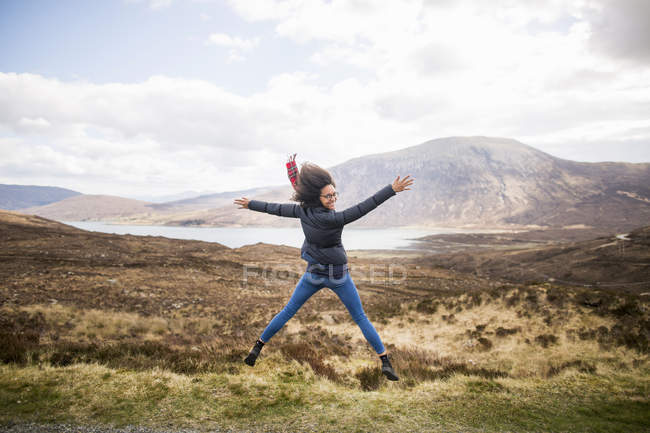 Mujer adulta en las montañas haciendo salto de estrella, Isla de Skye, Hébridas, Escocia - foto de stock