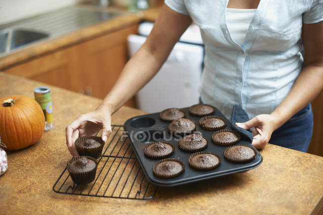 Mains féminines soulevant des gâteaux tasse sur rack de refroidissement — Photo de stock