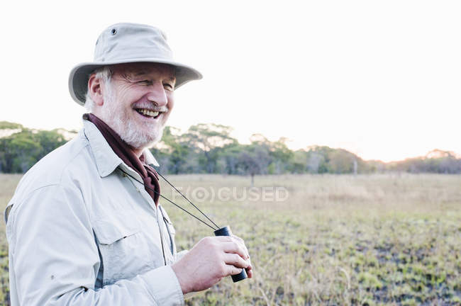 Hombre mayor sosteniendo prismáticos en safari, Parque Nacional Kafue, Zambia - foto de stock