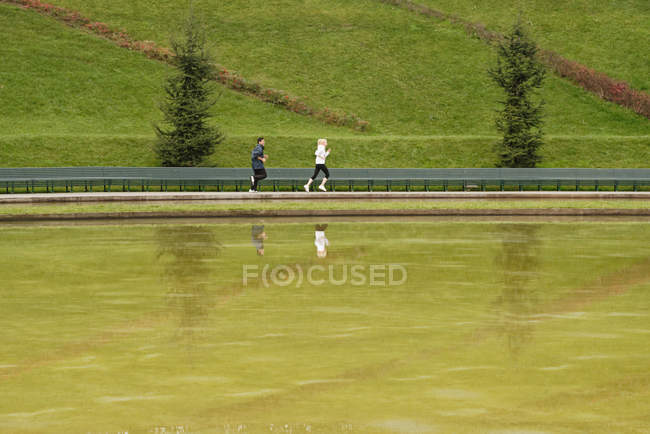 Man and woman running beside lake — Stock Photo