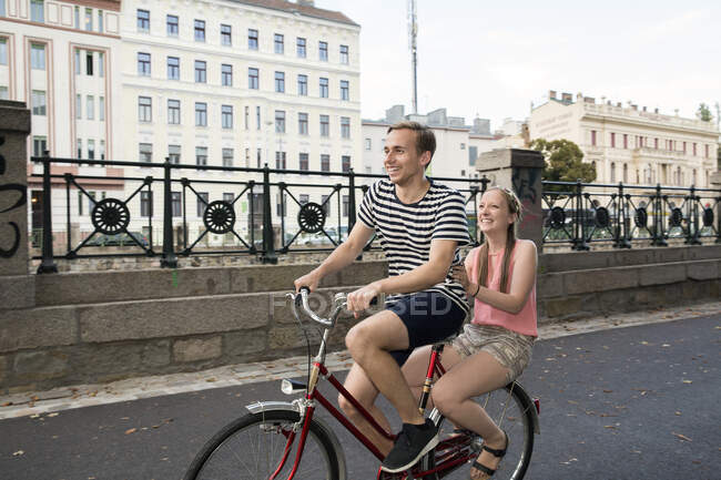 Young man riding bicycle with young woman sitting on back smiling — Stock Photo