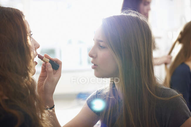 Teenage girl having lipstick applied by best friend in bedroom — Stock Photo