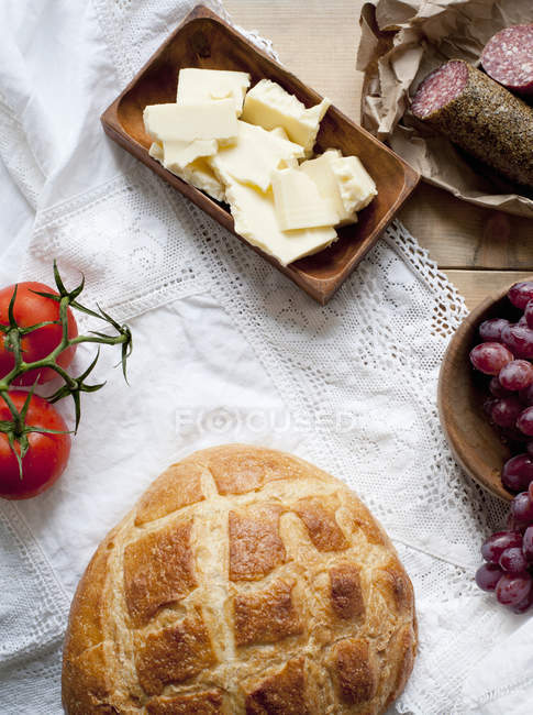 Bread, cheese, salami, grapes and tomatoes on table — Stock Photo