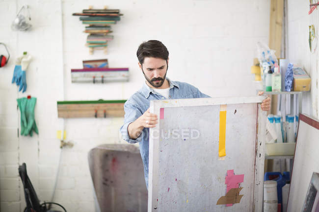 Young male printer looking at canvas in printing press studio — Stock Photo