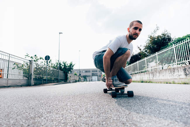 Giovane uomo accovacciato sullo skateboard — Foto stock