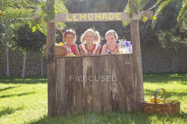 Retrato de tres chicas vendiendo limonada en el stand del parque - foto de stock