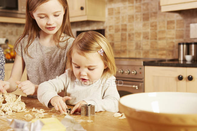 Femme tout-petit et grande sœur faisant pâtisserie en forme d'étoile à la table de cuisine — Photo de stock