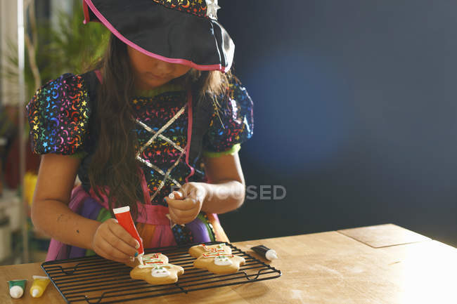 Girl wearing halloween witch costume decorating gingerbread men — Stock Photo