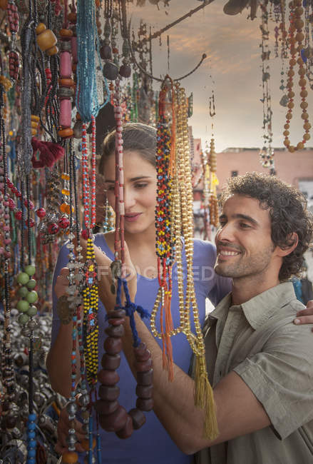 Parejas jóvenes en el mercado mirando perlas, Plaza Jemaa el-Fnaa, Marrakech, Marruecos - foto de stock