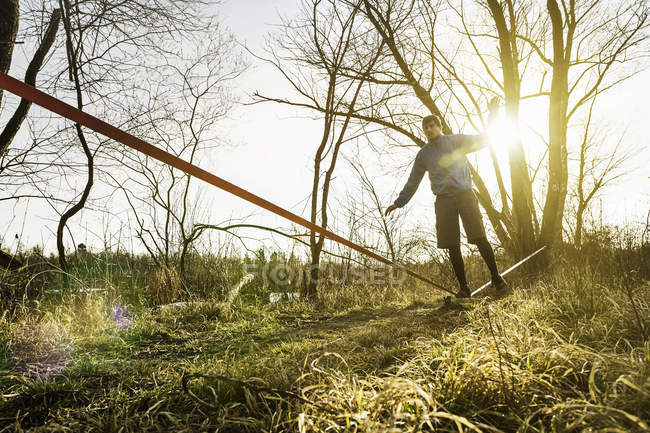 Молодой человек балансирует на одной ноге на вялой линии в полевом пейзаже — стоковое фото