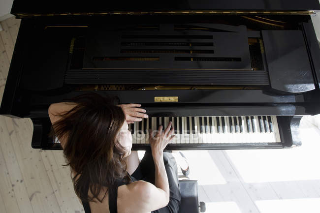 Vista aérea de una mujer madura apoyada en el piano tocando - foto de stock