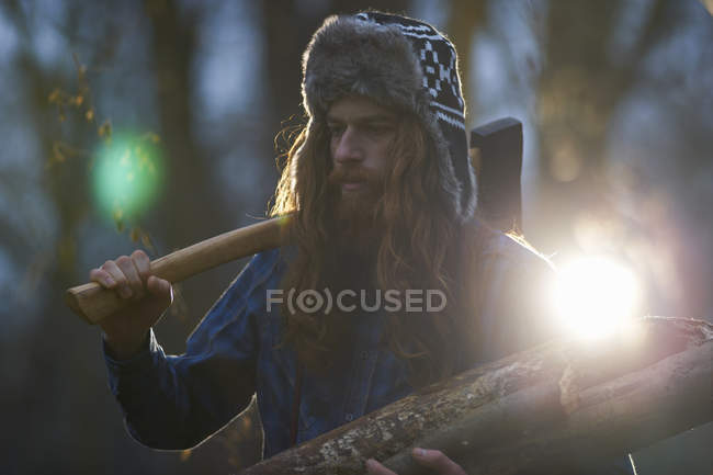 Man in trapper hat chopping wood in countryside — Stock Photo