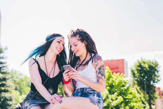 Две девушки смеются над смс-ками со смартфонов в городском жилом комплексе — стоковое фото