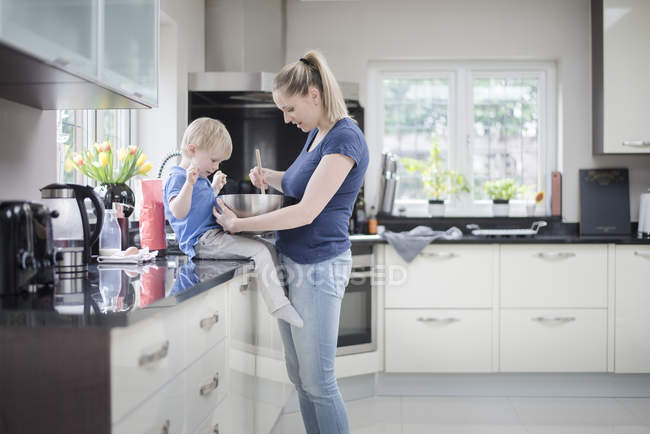 Мать и сын пекут вместе, перемешивая смесь в миске для смешивания — стоковое фото