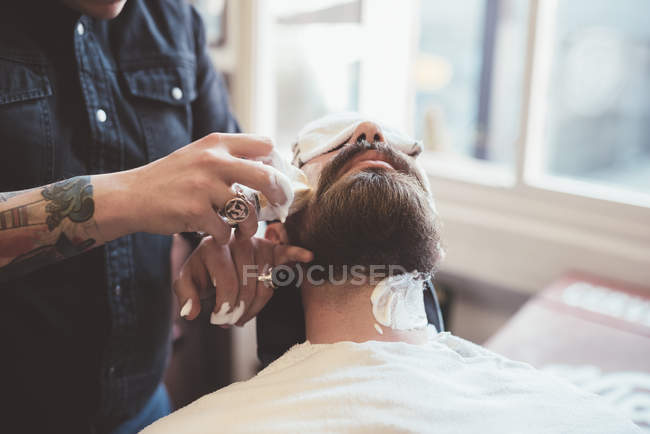 Peluquero aplicando crema de afeitar en la cara del cliente - foto de stock