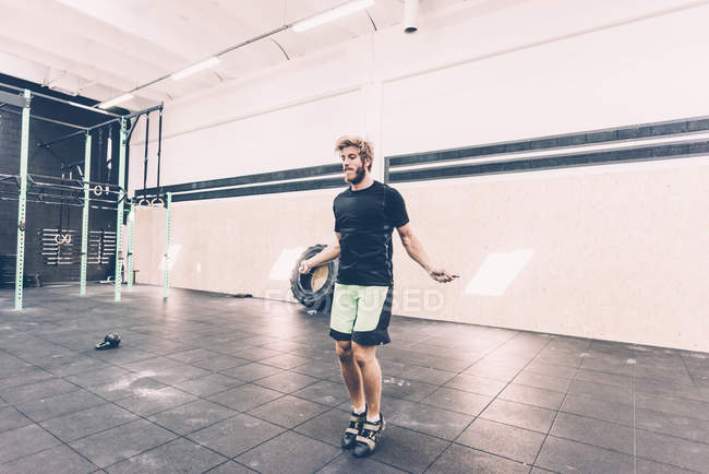 Jeune entraînement de cross-trainer masculin avec corde à sauter en salle de gym — Photo de stock