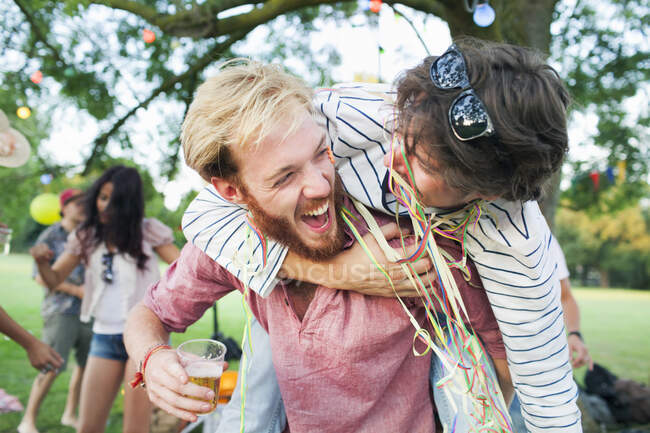Due amici adulti maschili avvolti in stelle filanti che si abbracciano al tramonto festa nel parco — Foto stock