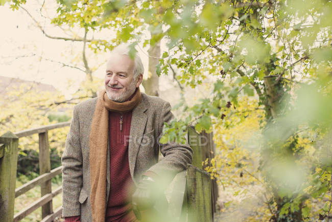 Hombre mayor sonriendo y apoyado en valla de madera - foto de stock