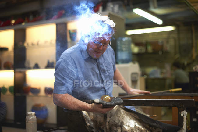 Glassblower in workshop forming molten glass on blowpipe — Stock Photo