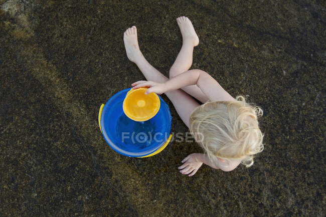 Vista aérea de una niña jugando en la arena con un cubo de juguete - foto de stock