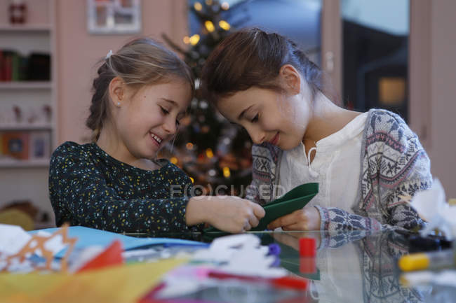Meninas à mesa fazendo artesanato de papel de natal sorrindo — Fotografia de Stock