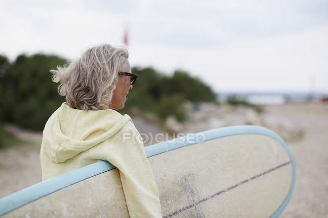 Seniorin läuft mit Surfbrett in Richtung Strand, Rückansicht — Stockfoto