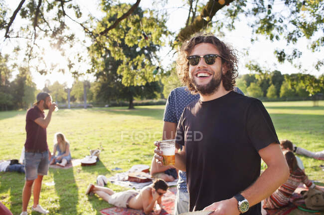 Portrait of young man drinking beer at group party picnic in park — Stock Photo