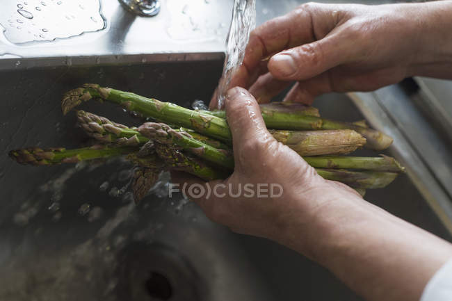 Обрезанный снимок человека, стирающего спаржу, сфокусированного на руках — стоковое фото