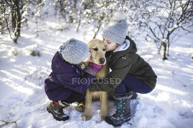 Deux jeunes filles, chien câlin, dans un paysage enneigé — Photo de stock