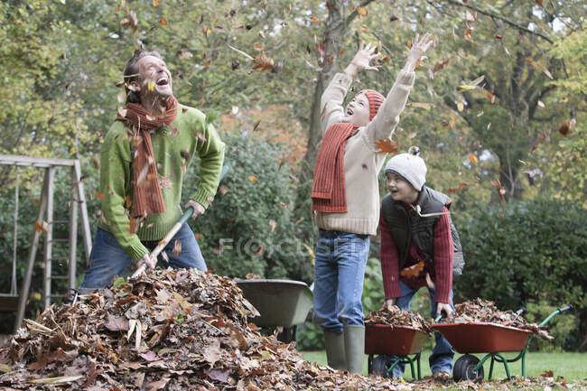 Father and sons fooling around in garden, gathering autumn leaves — Stock Photo