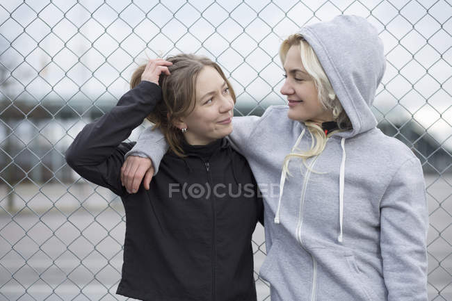 Two happy female runner friends by wire fence — Stock Photo