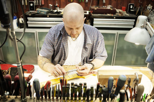 Производитель гитары измеряет шею гитары в мастерской — стоковое фото