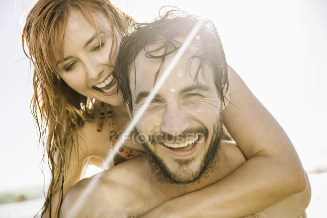 Retrato de homem adulto médio dando namorada piggyback na praia iluminada pelo sol, Cidade do Cabo, África do Sul — Fotografia de Stock