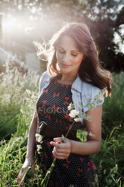 Frau pflückt Blumen auf sonnenbeschienener Wiese — Stockfoto