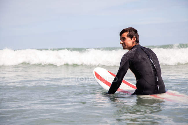 Jeune homme assis sur une planche de surf en mer — Photo de stock