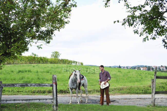 Junger Mann im Cowboy-Outfit führt Pferd durch Tor — Stockfoto