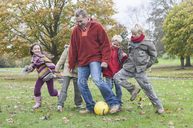 Pai e filhos, jogando futebol no parque — Fotografia de Stock