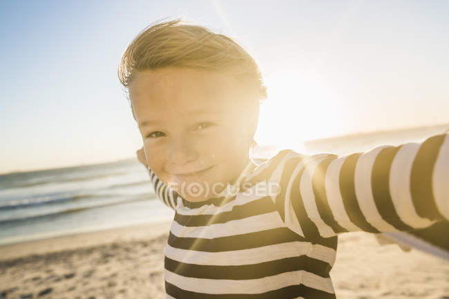 Porträt eines Jungen mit gestreiftem T-Shirt am Strand, der lächelnd in die Kamera blickt — Stockfoto