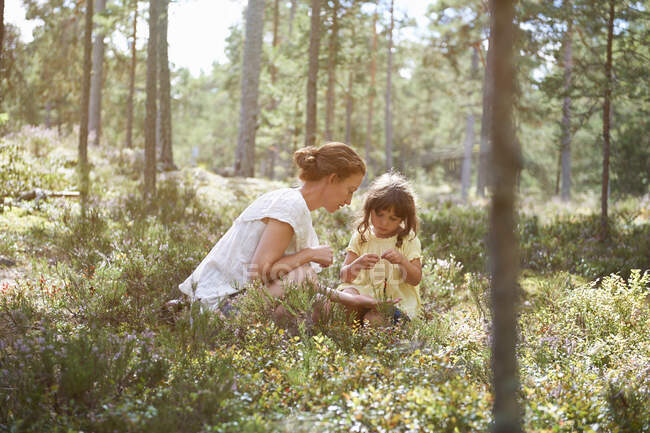 Мать и дочь сидят в траве и смотрят на растения. — стоковое фото