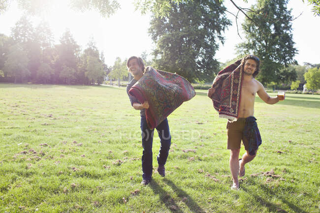 Two young men carrying rugs for sunset park party — Stock Photo