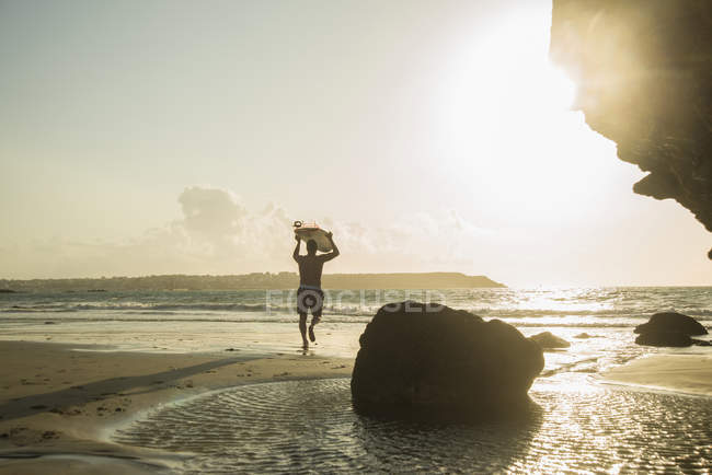 Зрілий чоловік біжить до моря, тримаючи дошку для серфінгу — стокове фото