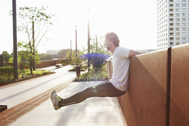Homem treinando levantando as pernas na ponte urbana — Fotografia de Stock