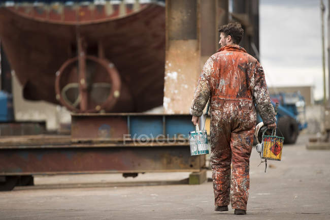 Visão traseira do pintor de navio masculino transportando latas de tinta no estaleiro de pintores de navio — Fotografia de Stock