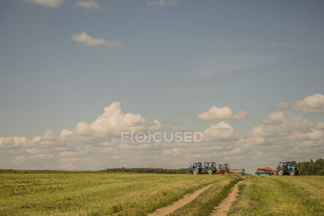 Tracteurs récolte champ sous ciel nuageux bleu — Photo de stock