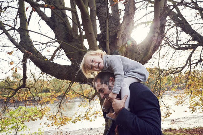 Отец носит дочь на плечах в осеннем парке — стоковое фото