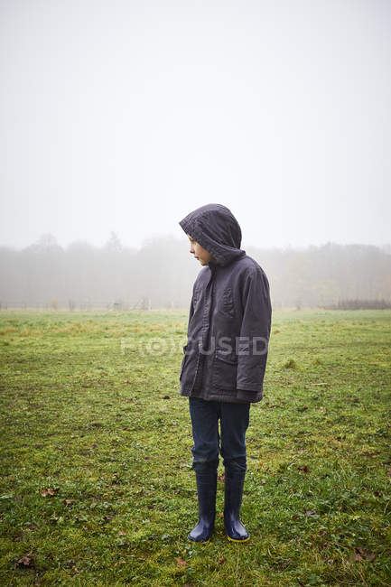 Мальчик в пальто стоит на зеленом поле — стоковое фото