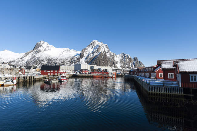 Casas frente al mar y montañas nevadas bajo el cielo azul claro - foto de stock